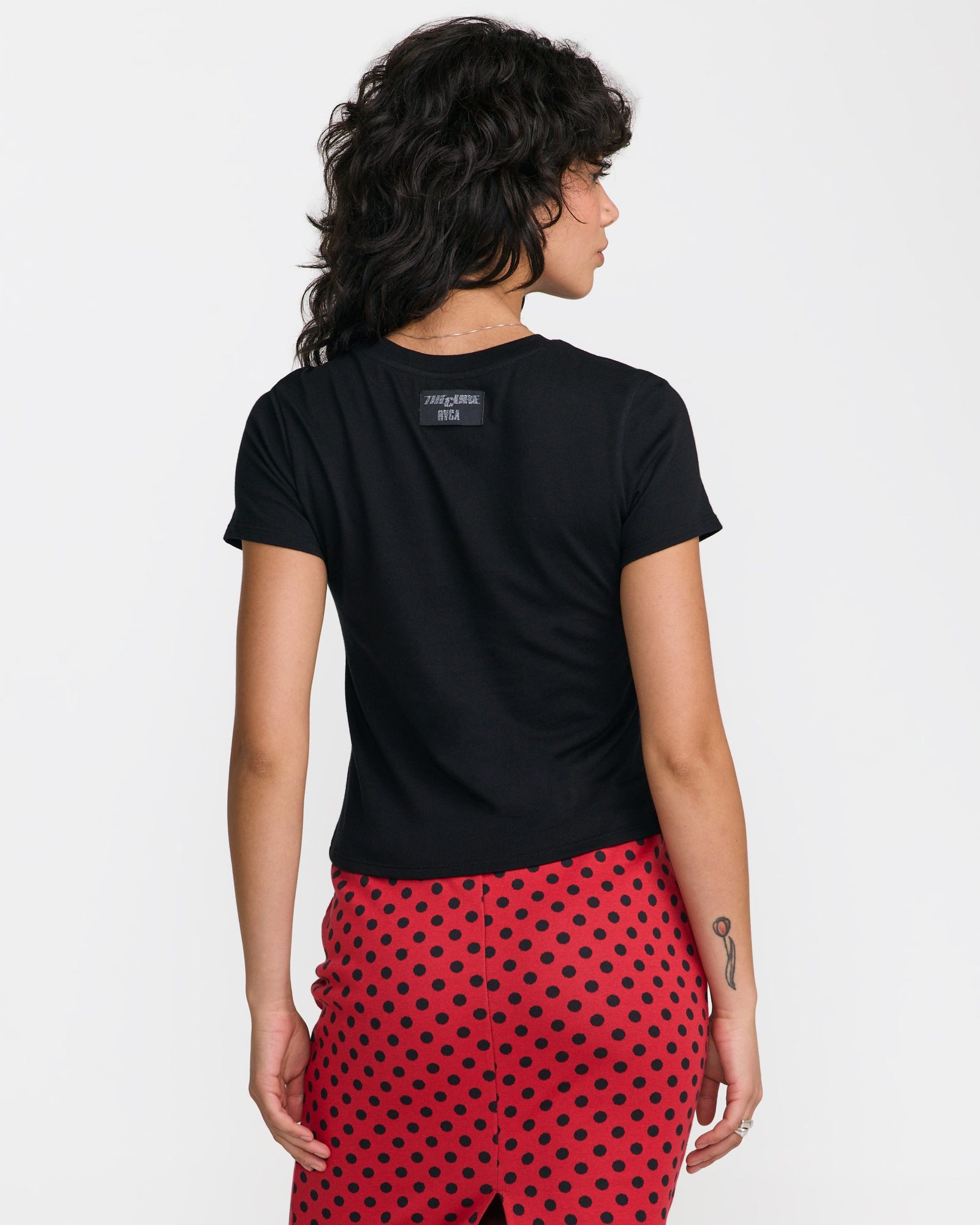 Woman from behind wearing black t-shirt with back logo and red polka dot pants