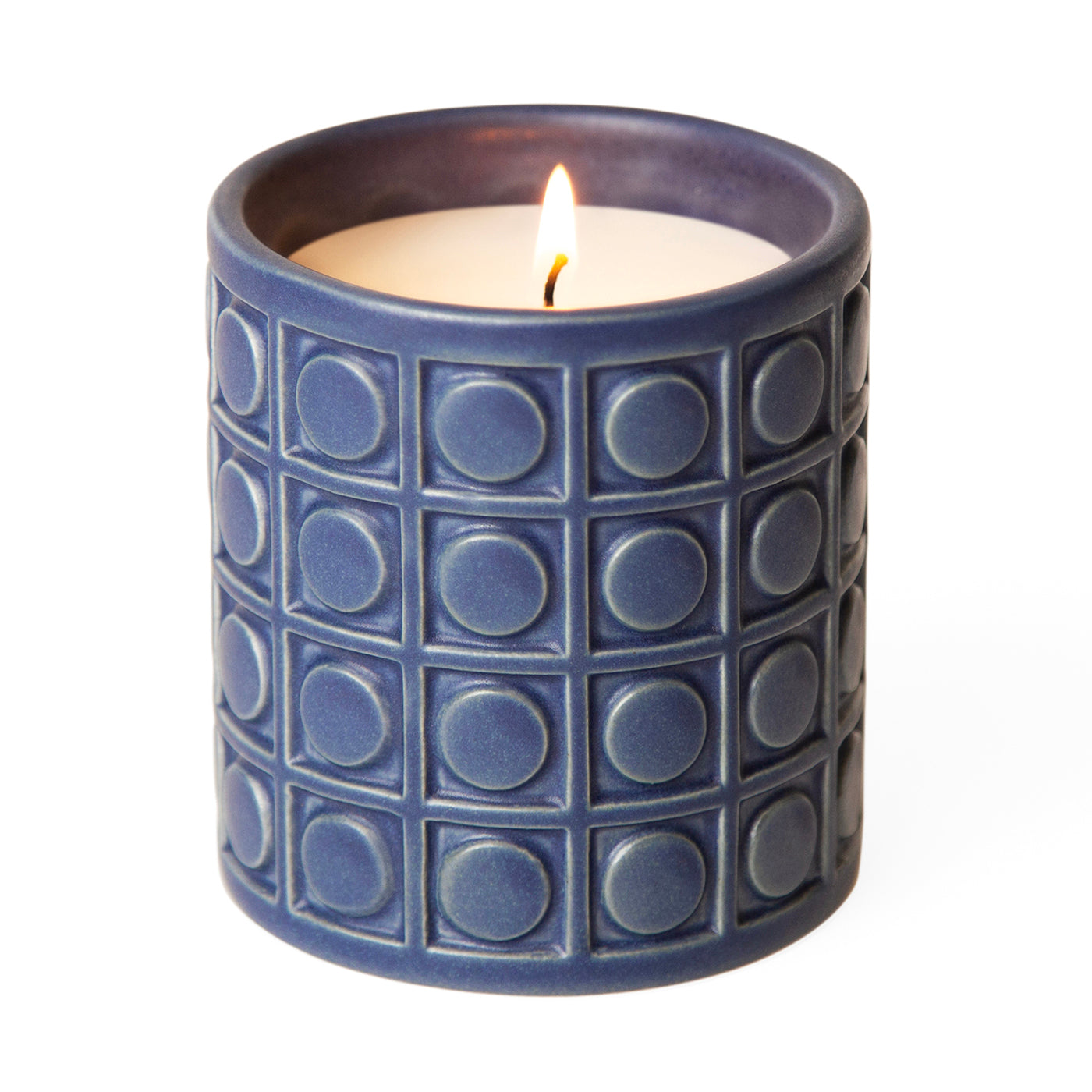 Blue ceramic candle with geometric circle and square pattern, lit with glowing yellow flame