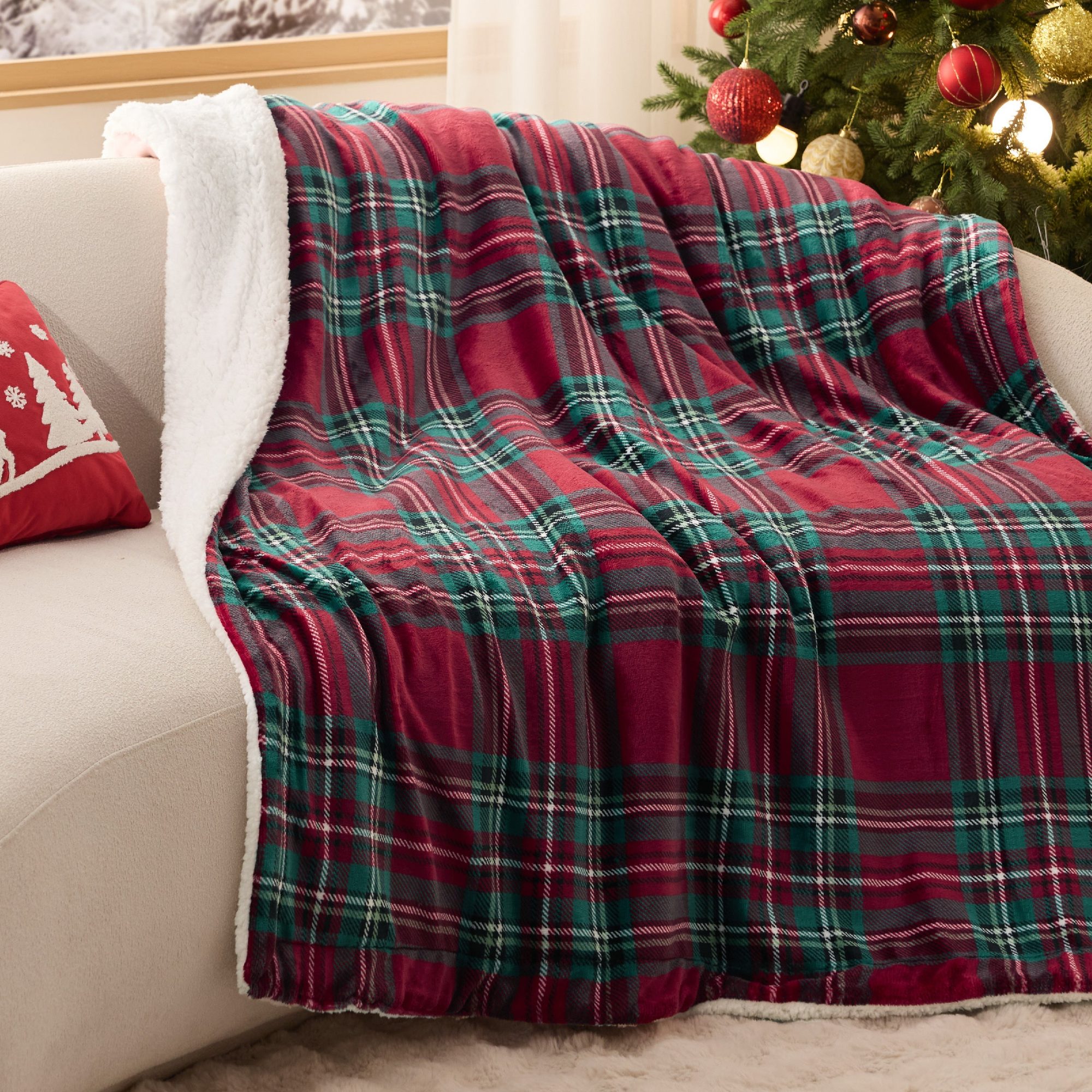 Red and green plaid blanket with white fleece lining draped over cream sofa arm by Christmas tree