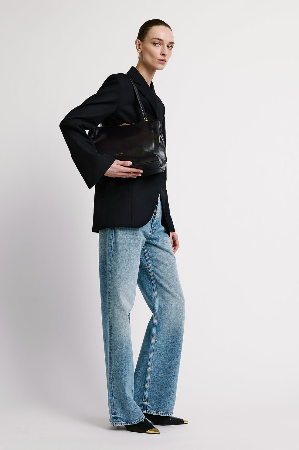 Woman wearing black blazer with light blue jeans and black pointed-toe shoes, holding black leather shoulder bag
