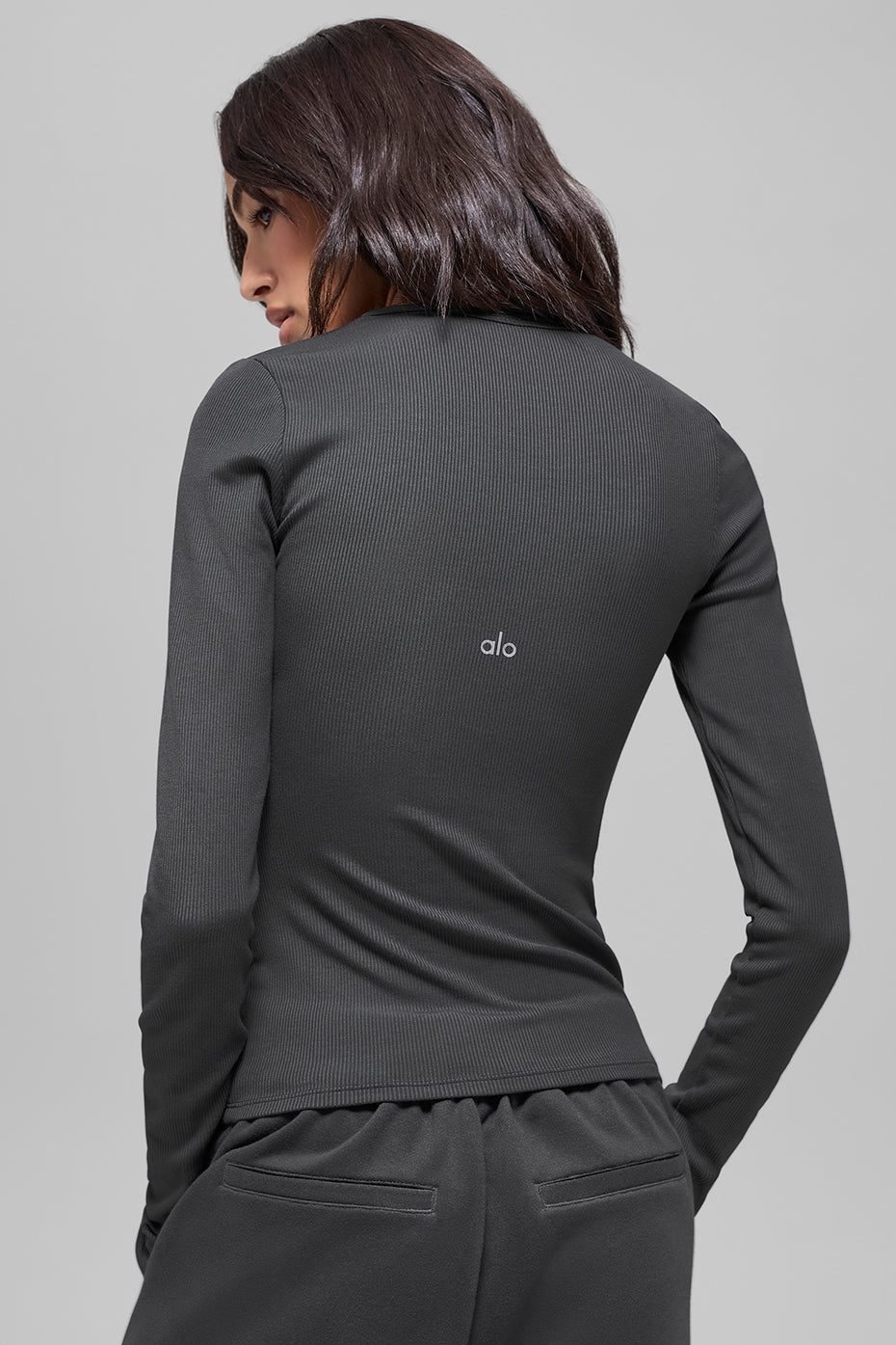 Back view of woman in charcoal ribbed long-sleeve top with Alo logo, paired with black jogger pants with pocket detail