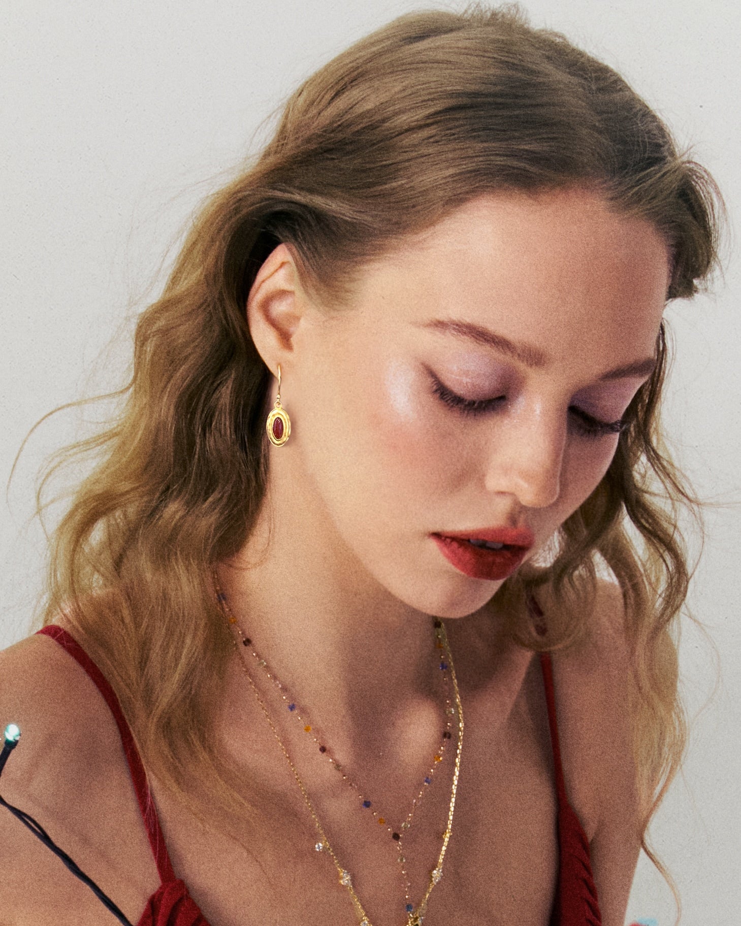 Woman in profile wearing the gold oval red stone earring, looking downward with wavy hair