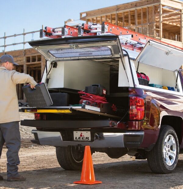 Man loading tools into open red pickup truck bed with roof-mounted storage rack at construction site