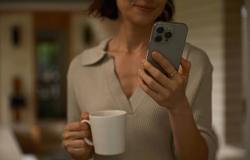 Woman holding smartphone and white mug indoors
