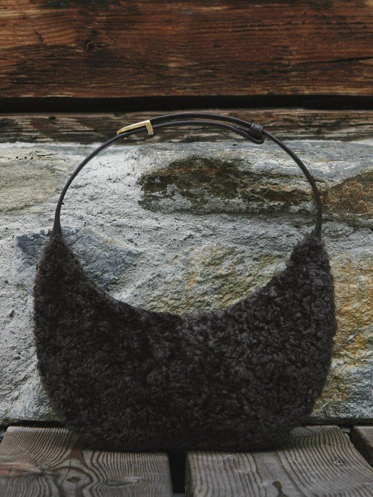 Black textured knit hobo bag with leather handle displayed on stone surface