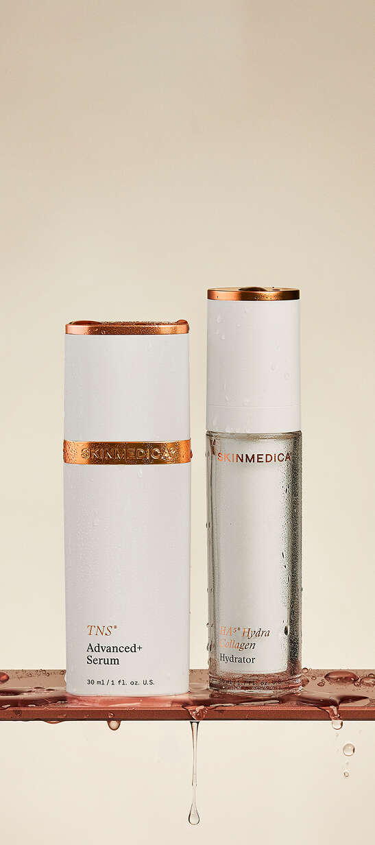 Two white bottles with copper bands containing serum and hydrator on bronze surface with water droplets