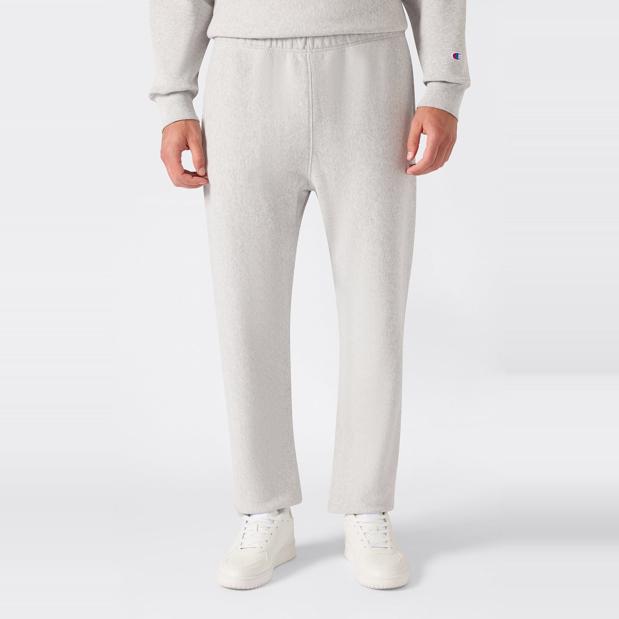 Man wearing cream-colored sweatpants with small embroidered logo, cropped detail view