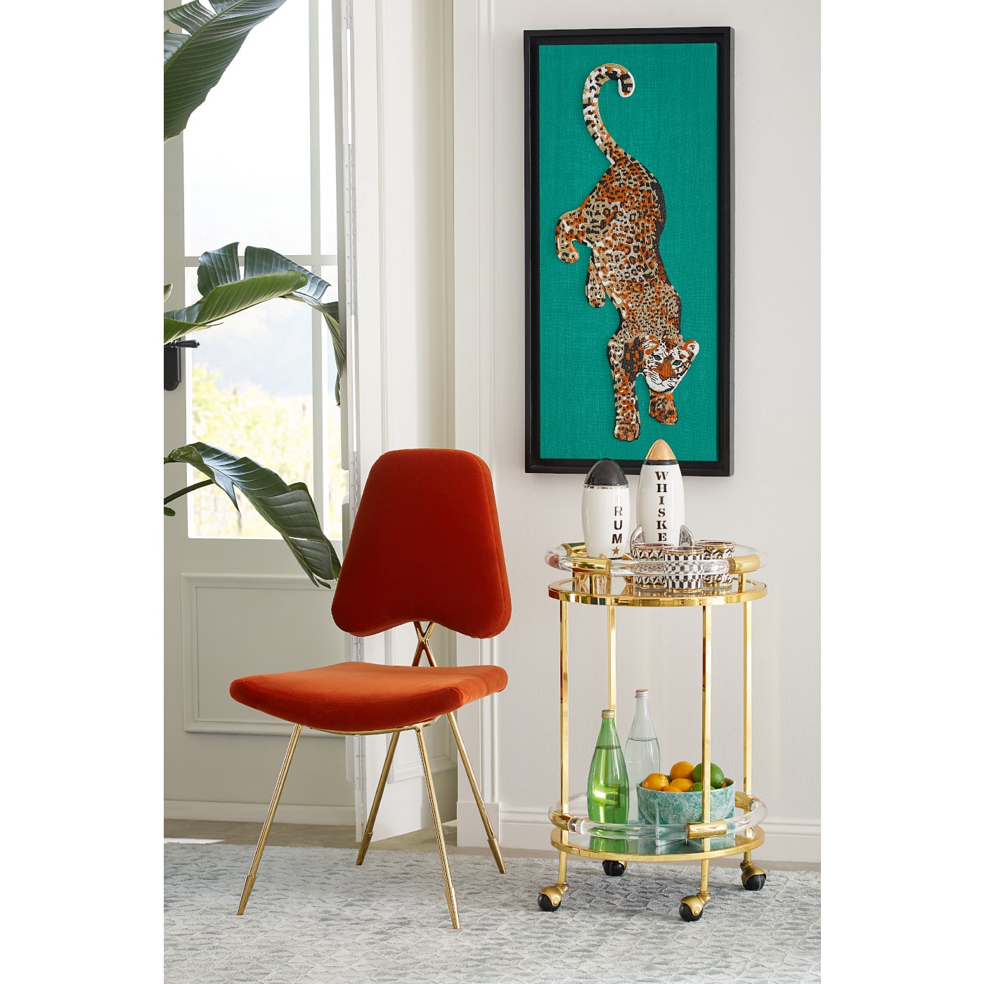 Interior scene with framed leopard artwork above gold side table with red velvet chair