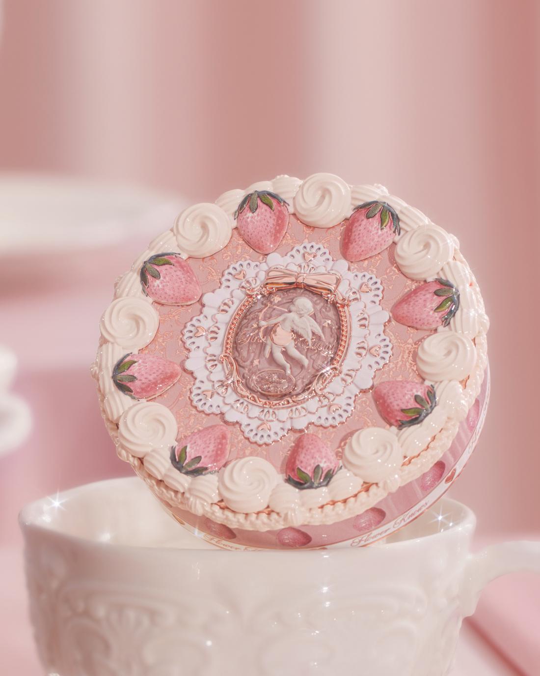 Decorative round makeup compact with strawberry and floral design on white pedestal against pink background
