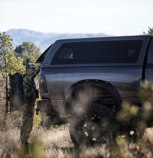 Black lifted pickup truck with tonneau cover parked on dusty terrain with mountains in background