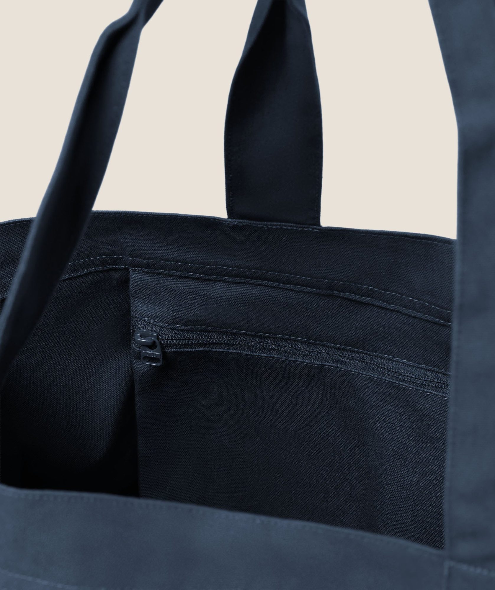 Close-up of navy canvas tote bag showing handles and front zipper pocket detail