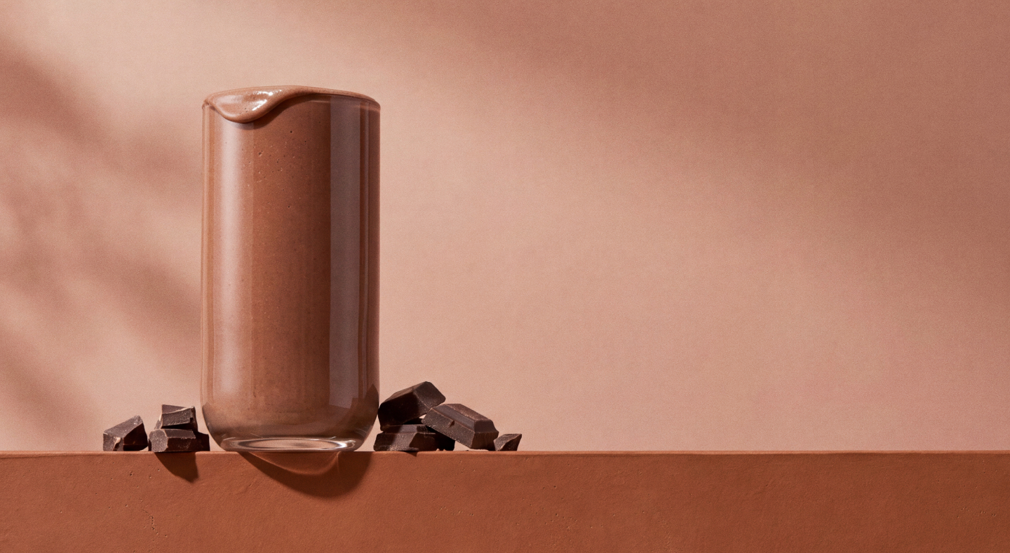 Glass of chocolate shake with cocoa pieces scattered beside it on brown surface