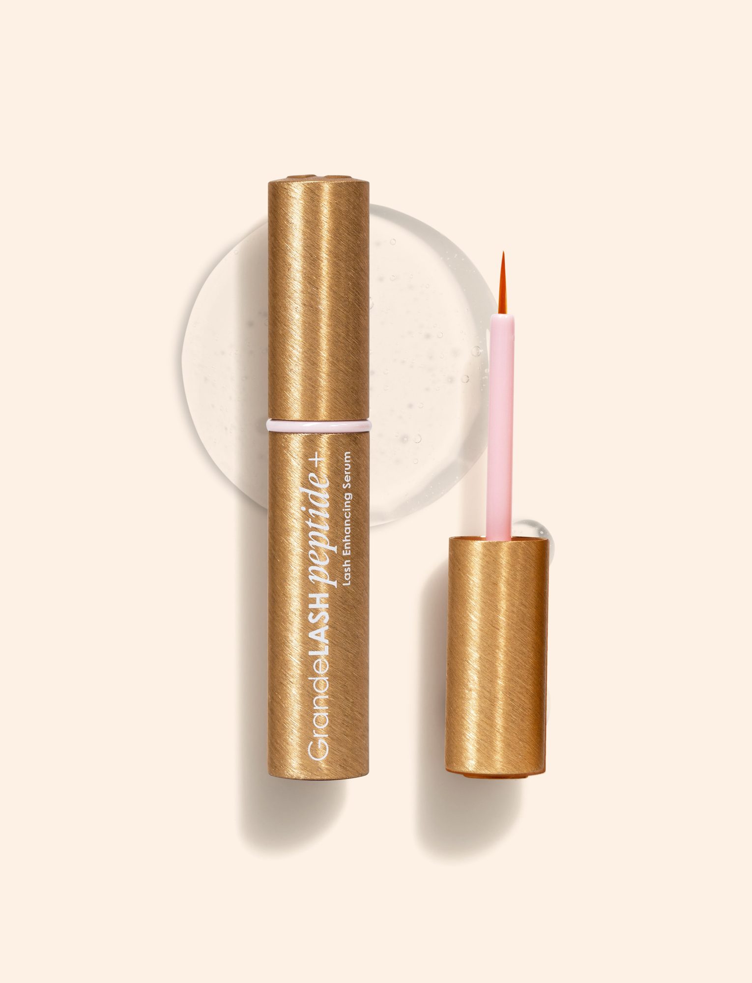 Gold tube lash enhancing serum with pink applicator wand and white circular backdrop