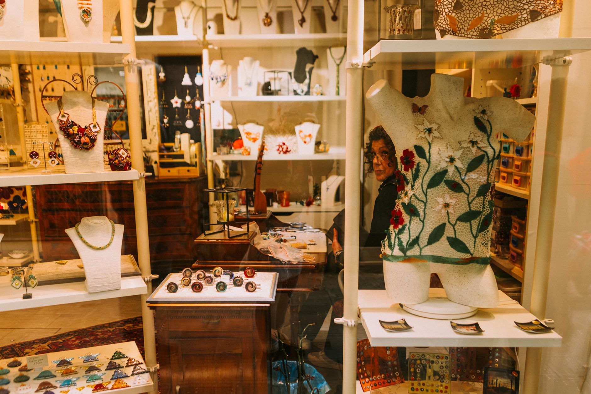 Jewelry store display with necklaces, earrings, and embellished clothing on white shelving and mannequins