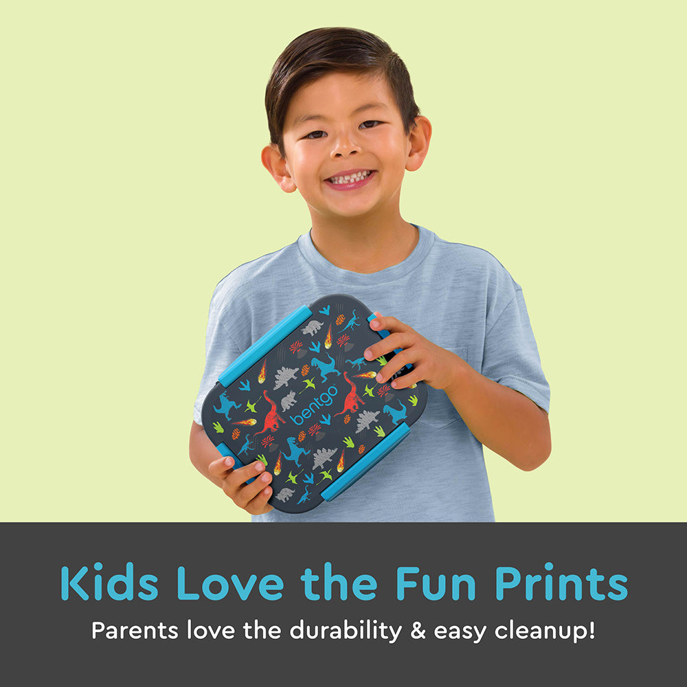 Young boy smiling while holding closed dinosaur-patterned lunch box against his chest