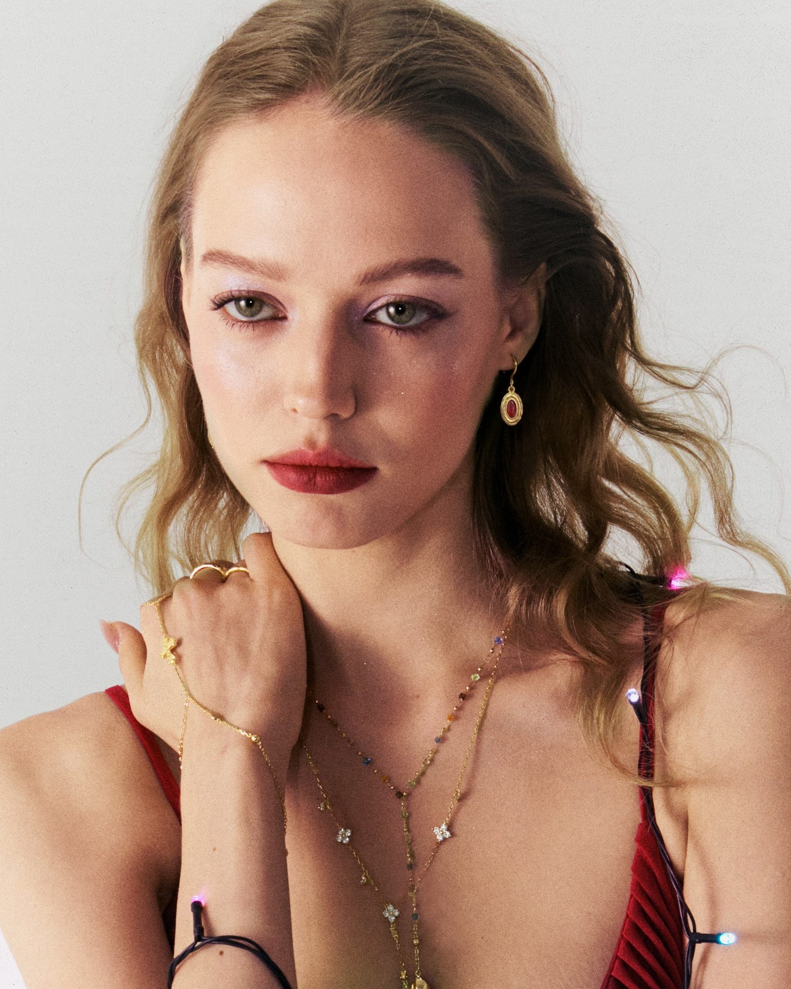 Woman with wavy brown hair wearing gold oval earring with red stone and delicate chain necklaces