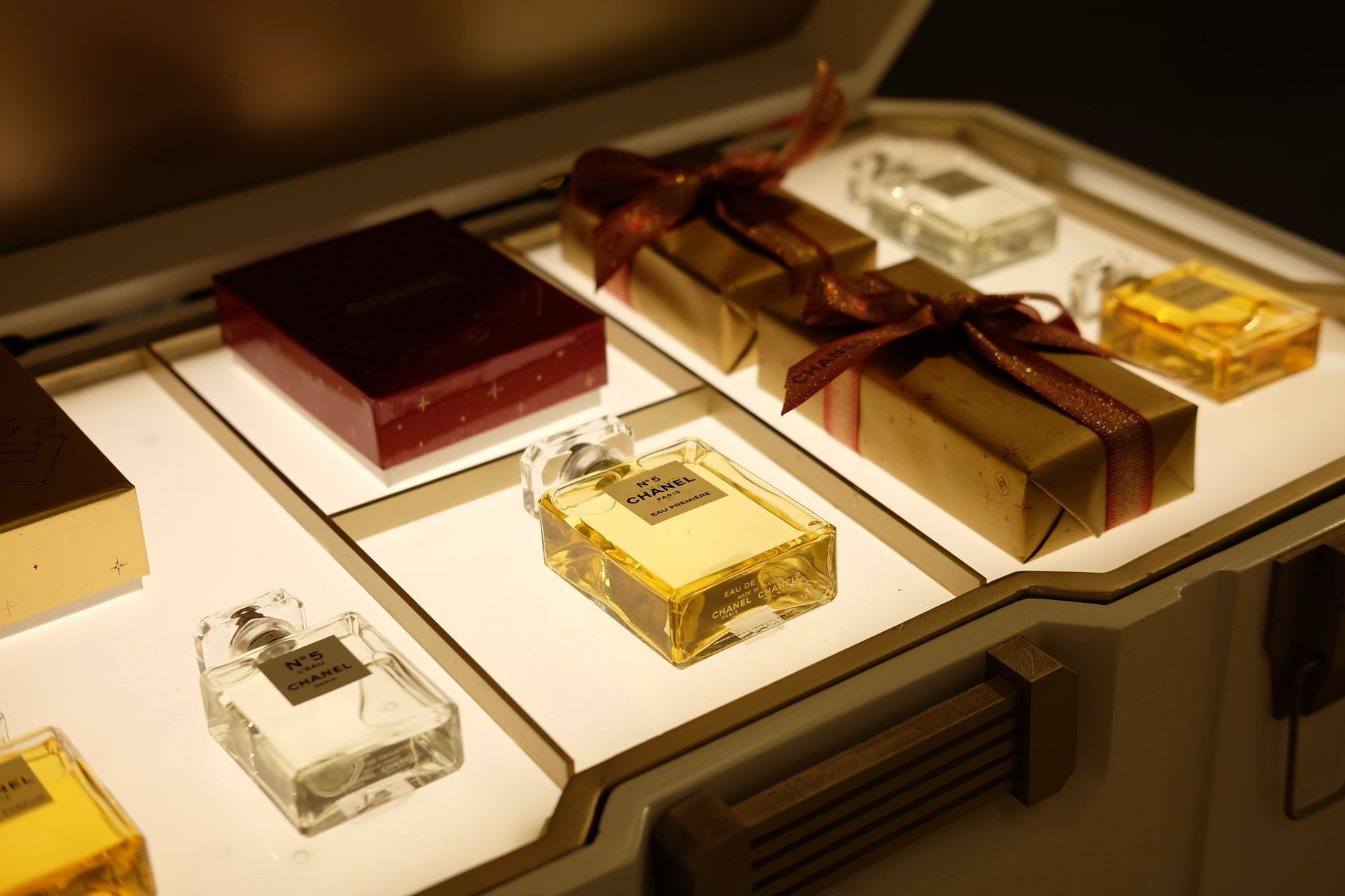 Luxury beauty products display including perfume bottles and wrapped gift boxes with decorative ribbons on illuminated shelf