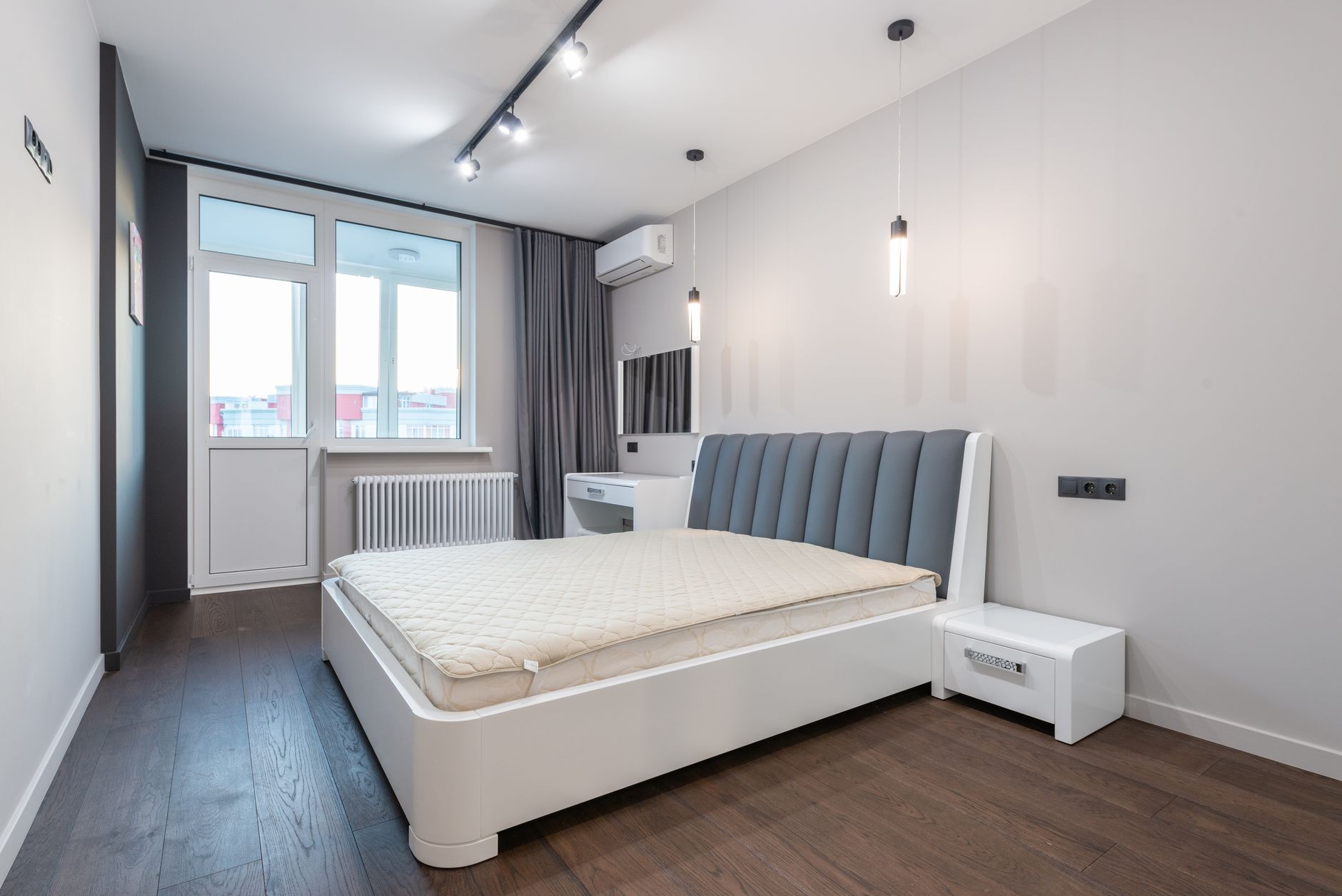 Modern bedroom with white bed, gray headboard, pendant lights, and wall-mounted air conditioning unit