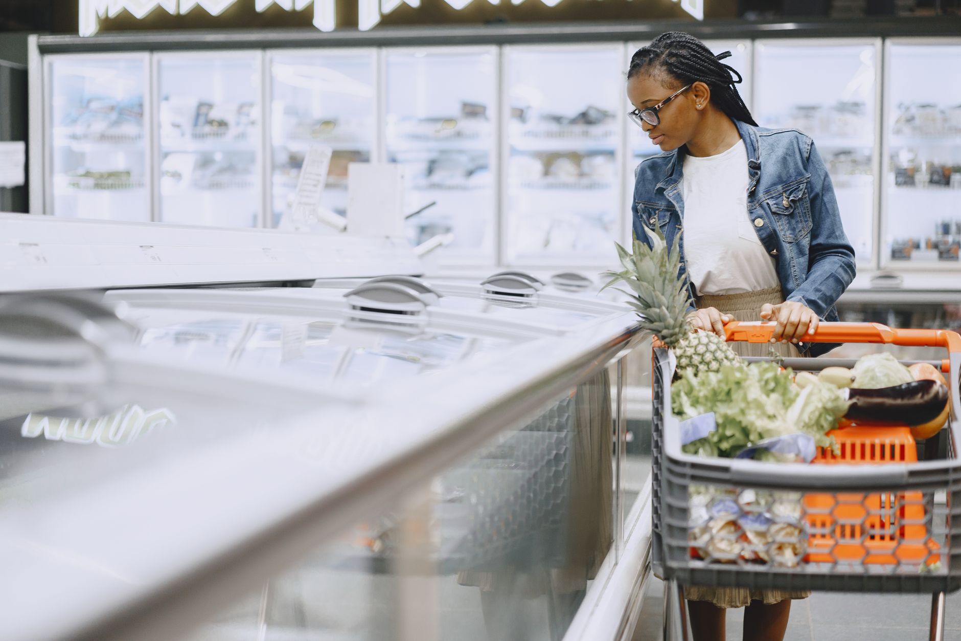 Woman shopping in produce section at warehouse, selecting pineapple and vegetables with shopping cart
