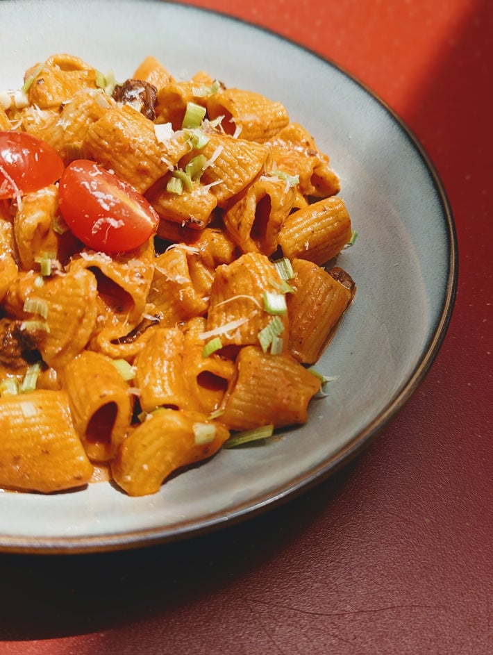 Bowl of pasta tubes with red sauce, tomatoes, and green onion garnish