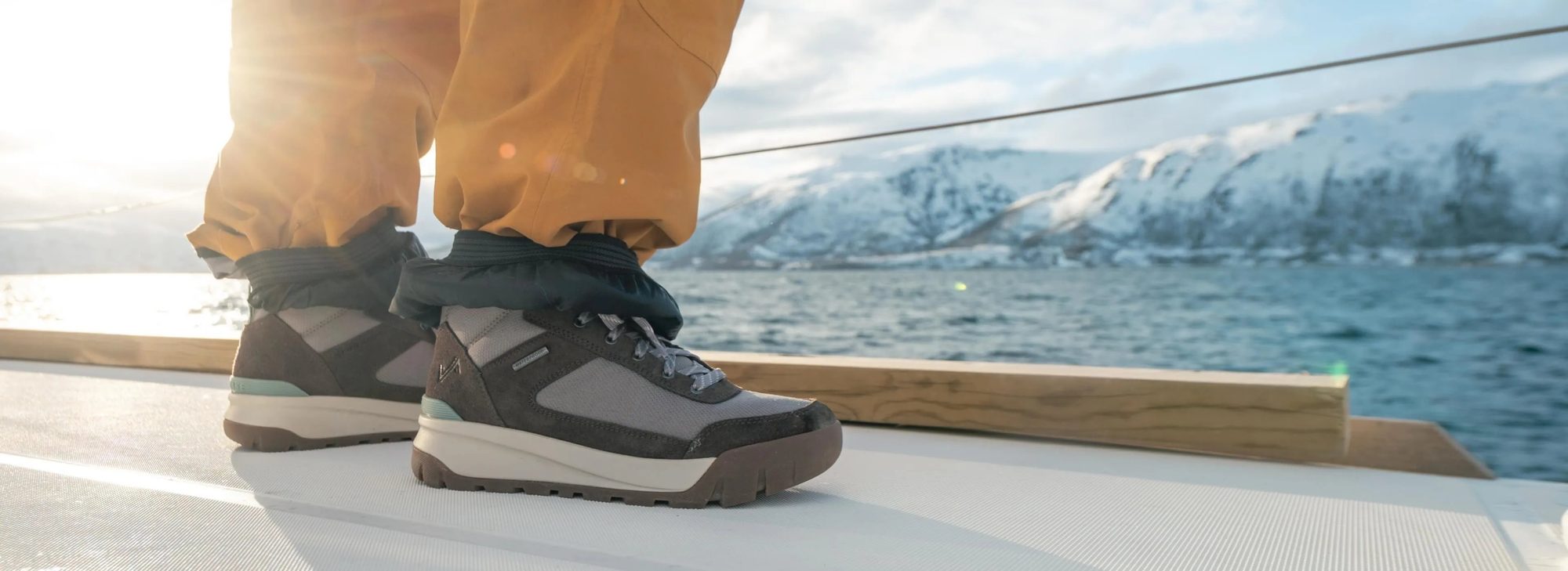 Person wearing black and gray hiking boots on a boat deck with snowy mountains in the background