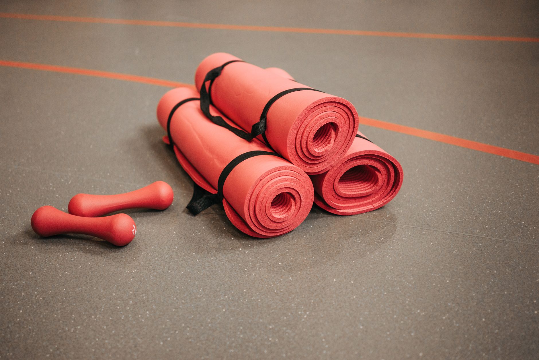Red rolled yoga mats bundled with black straps and red hand weights on dark floor