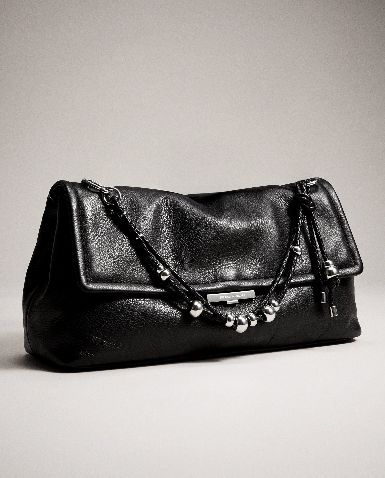 Black pebbled leather clutch with silver chain and beaded strap on neutral background