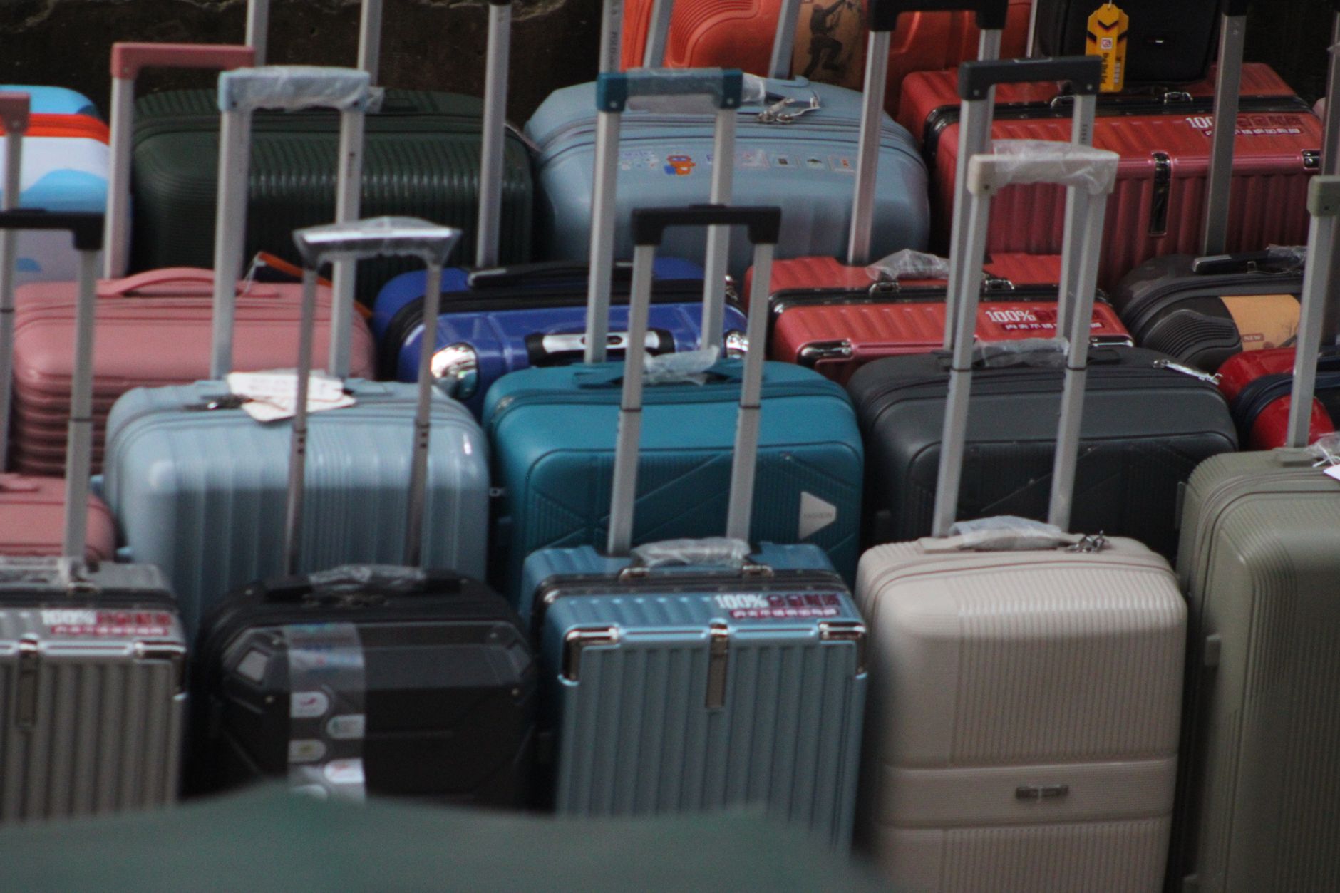 Overhead view of packed rolling luggage in multiple colors including light blue, teal, navy, red, pink, and beige arranged tightly together at what appears to be a travel or storage facility