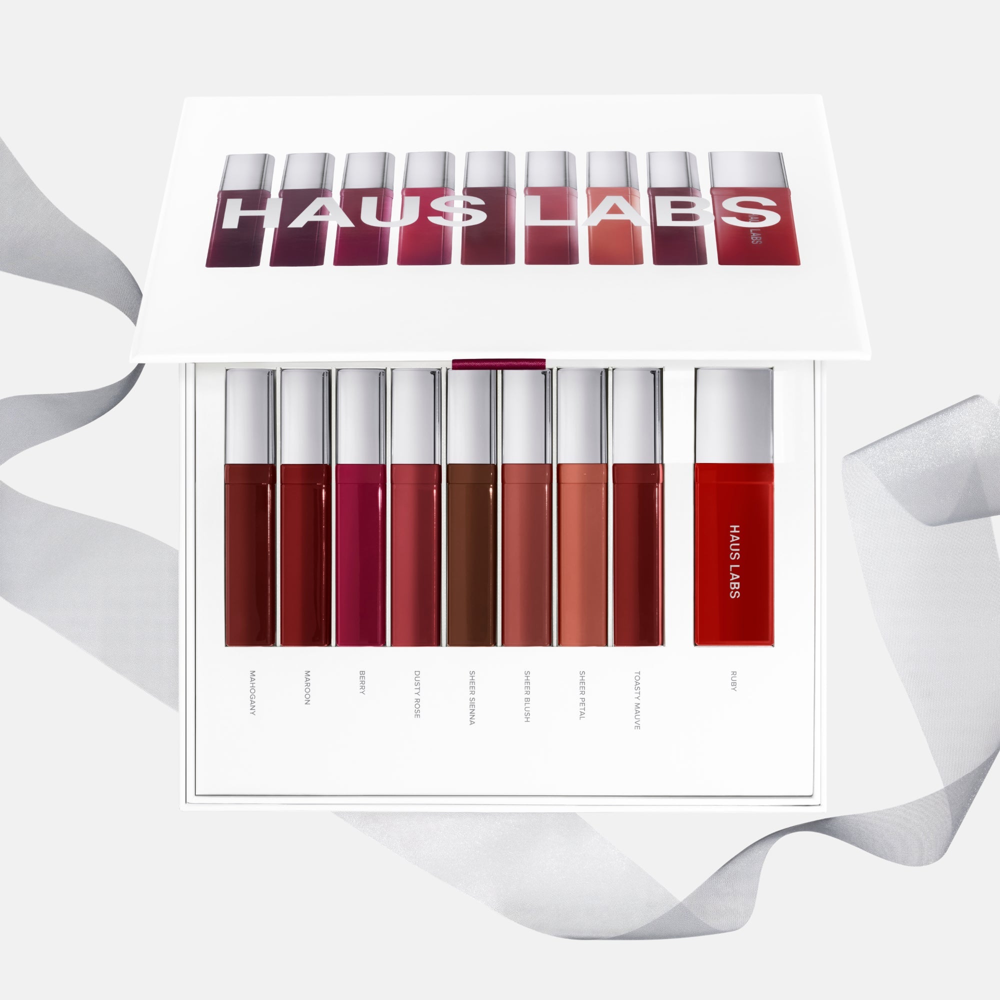Open product set showing nine liquid lipstick tubes in different red and burgundy tones with shade names labeled below each bottle