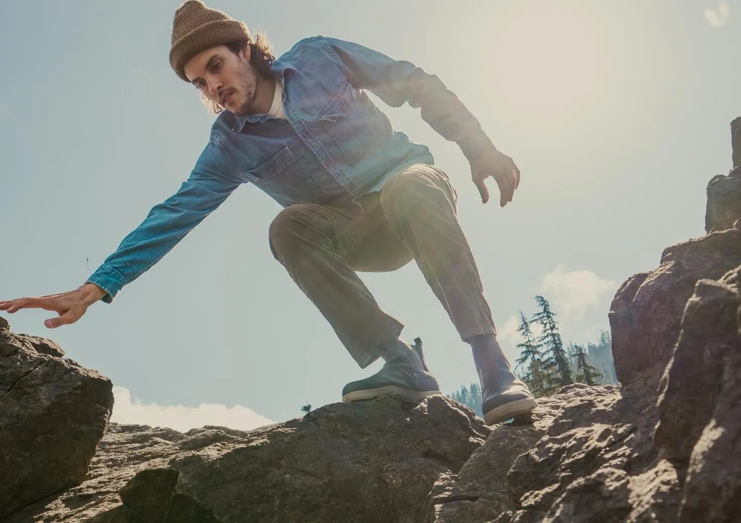 Man in denim shirt jumping between rocks with mountains and trees visible in the background