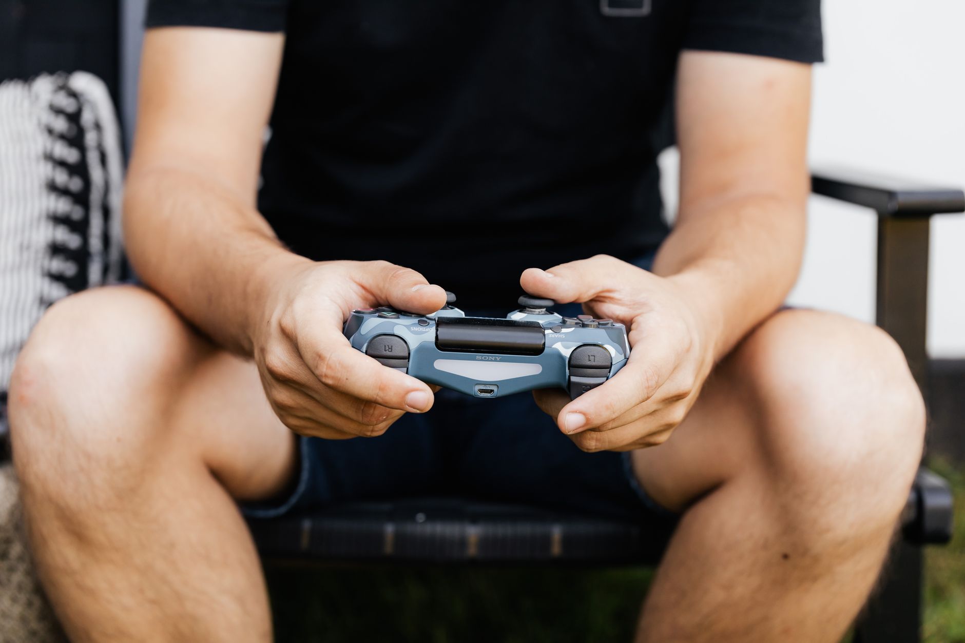 Person in black shirt holding blue gaming controller while sitting