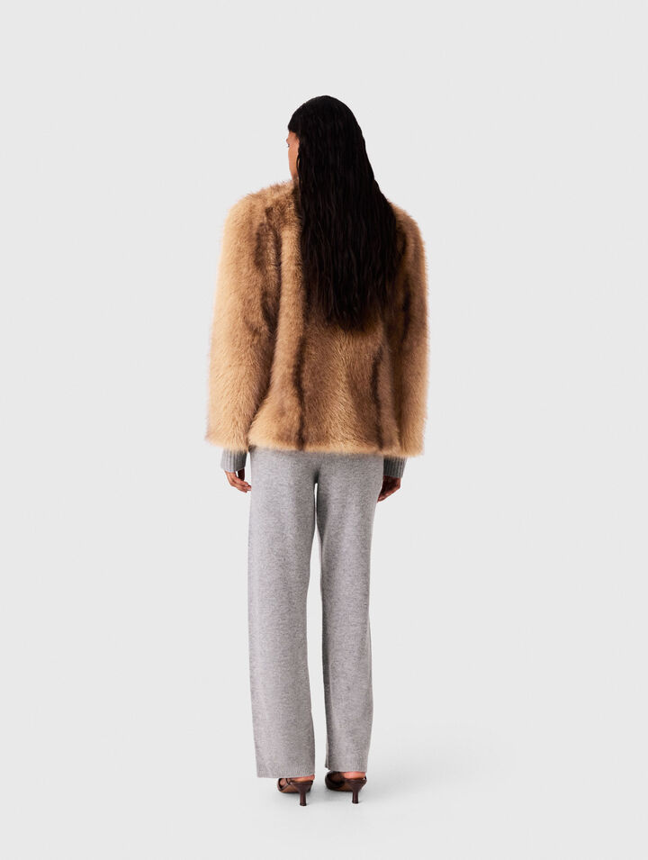 Woman wearing camel fur jacket and gray trousers, viewed from behind