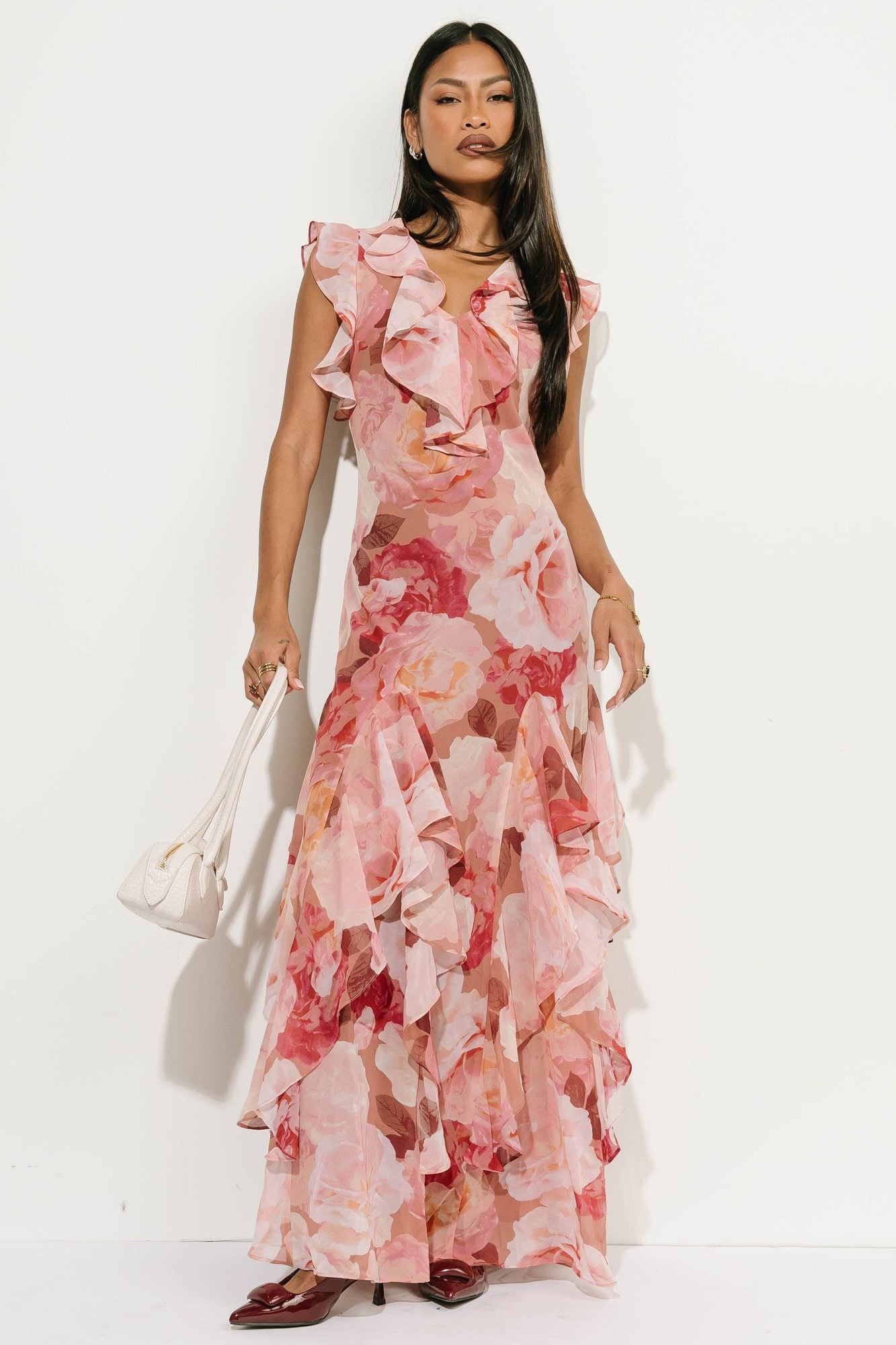 Woman in pink floral ruffle dress with ruffled neckline, holding white handbag
