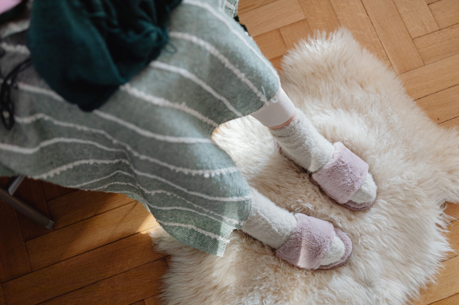 Person wearing cozy pink and white fuzzy slippers while sitting on a cream-colored fluffy rug