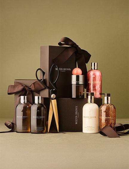 Luxury gift set with beauty and personal care products including bottles, soaps, and accessories arranged with brown ribbon and packaging