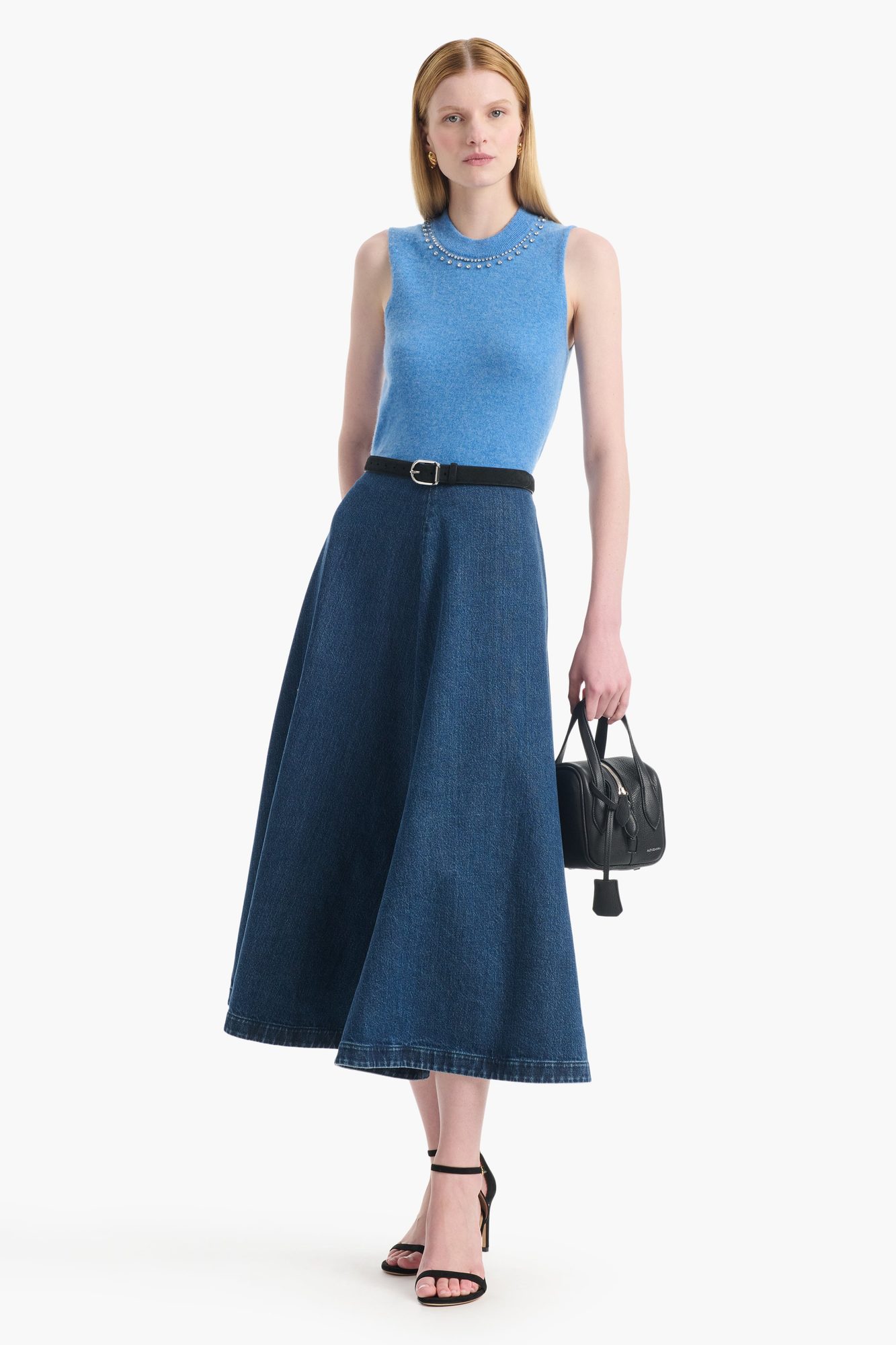 Woman wearing light blue sleeveless sweater with pearl neckline over dark denim midi skirt
