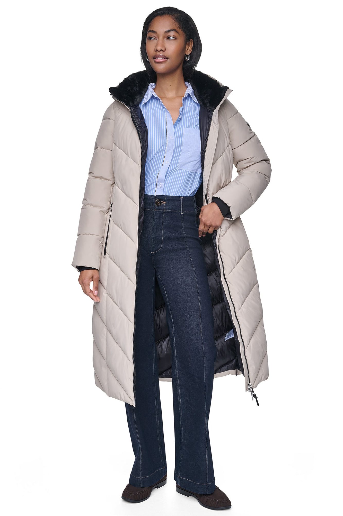 Woman in beige puffer coat with black fur collar worn open over blue striped shirt and dark jeans
