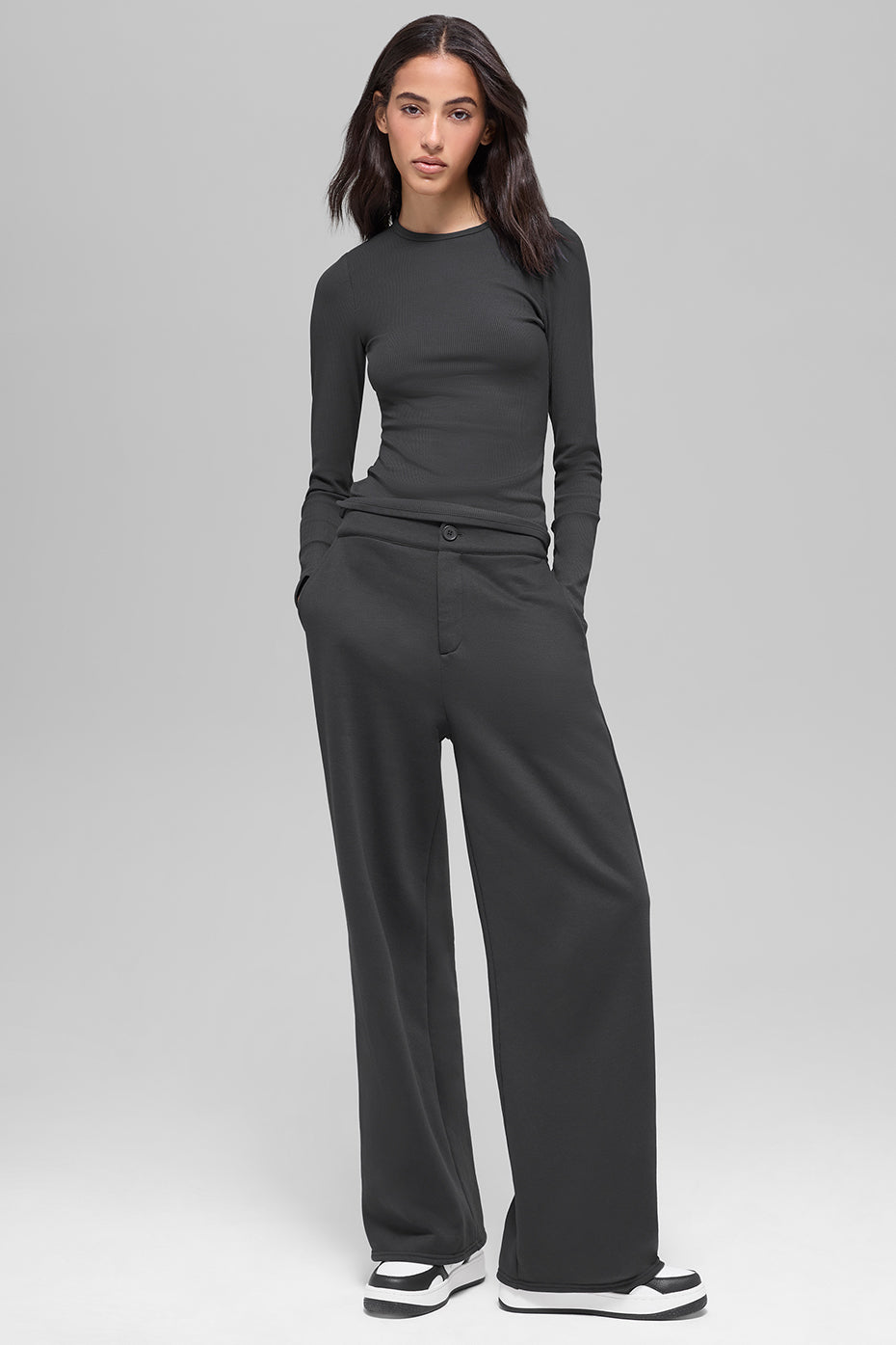 Woman wearing charcoal ribbed long-sleeve crew neck top tucked into high-waisted black wide-leg trousers with white sneakers