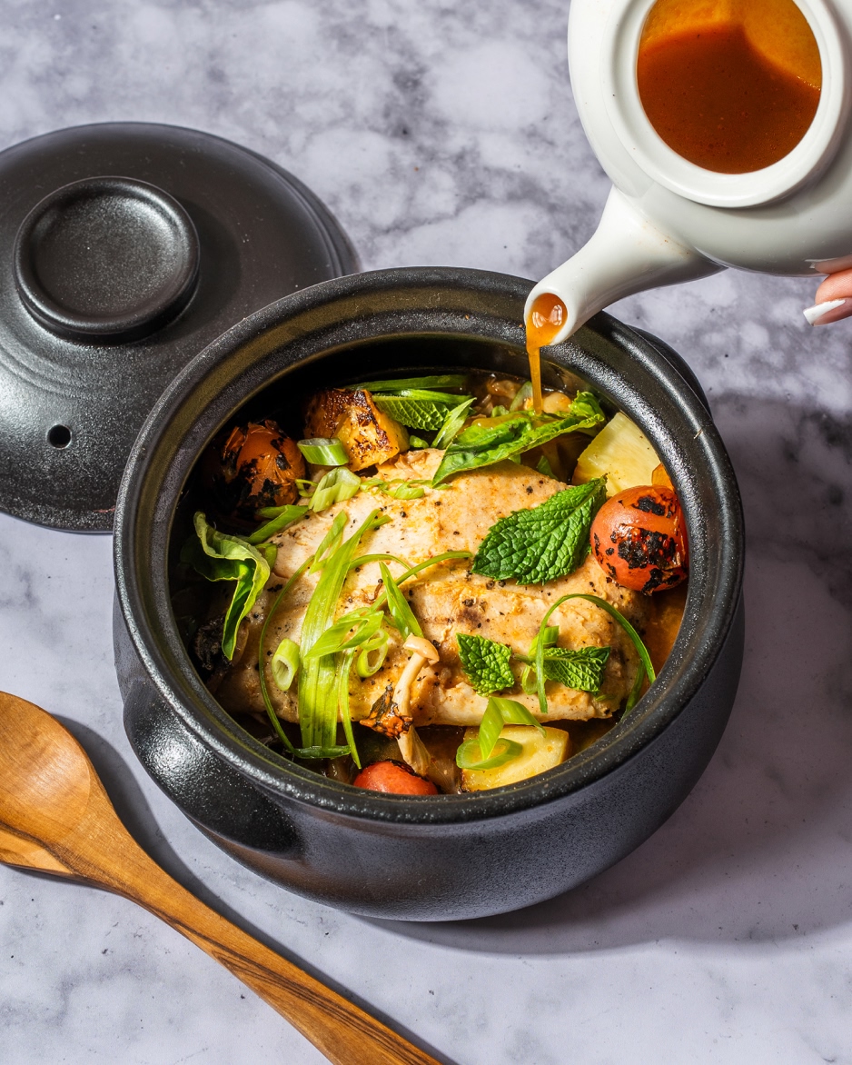 Asian fusion soup with salmon, vegetables, and green onions in a black ceramic bowl