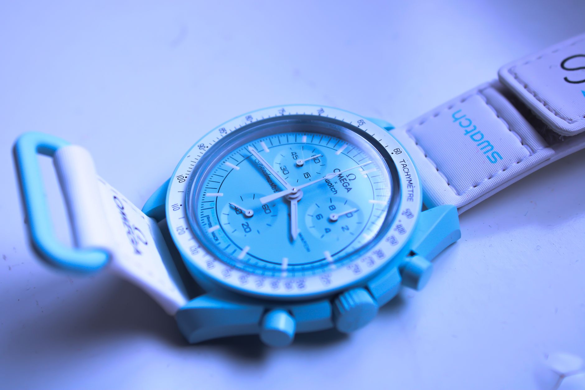 Blue chronograph watch with textile strap on purple background, angled product shot