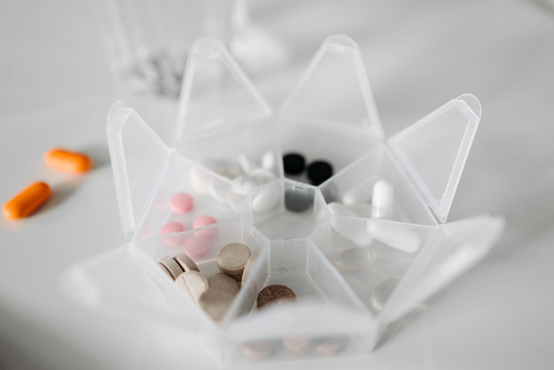 White star-shaped pill organizer with various medications and supplements including orange capsules, pink tablets, black pills, and beige supplements