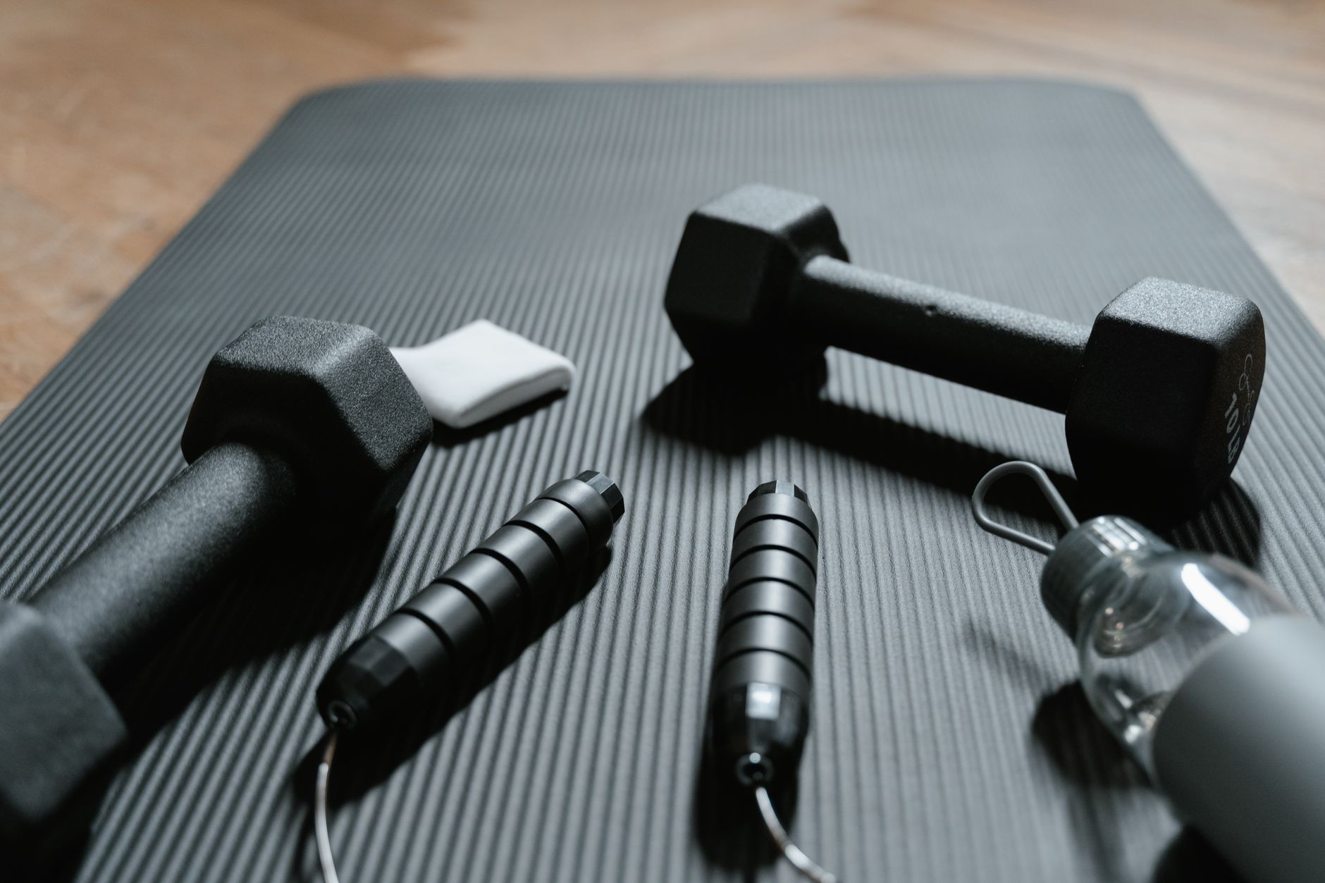 Fitness equipment arranged on gray mat including dumbbells, jump ropes, and water bottle