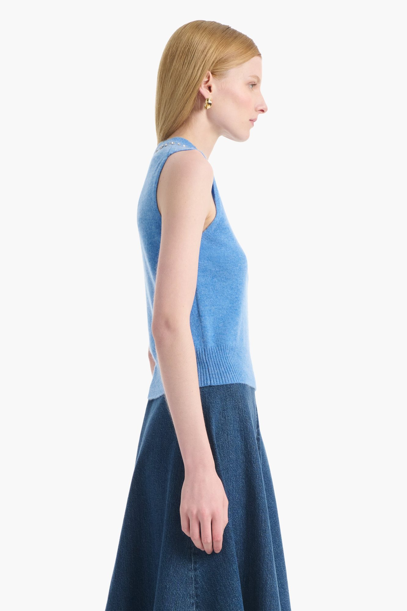 Side view of woman in light blue sleeveless sweater with pearl neckline and dark denim skirt