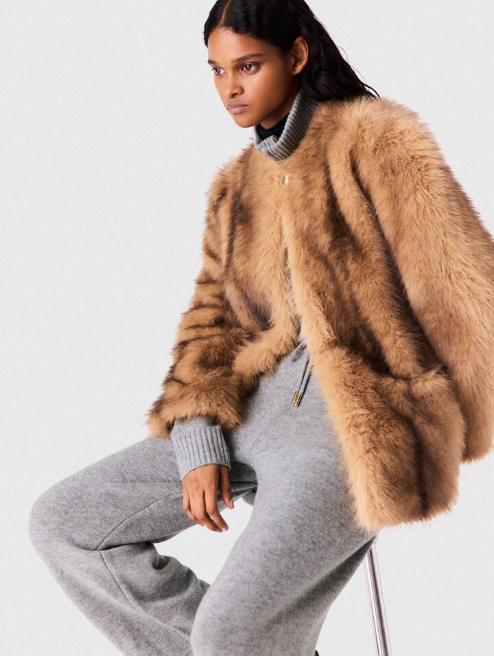 Woman in camel fur jacket and gray sweatpants, seated pose, side angle