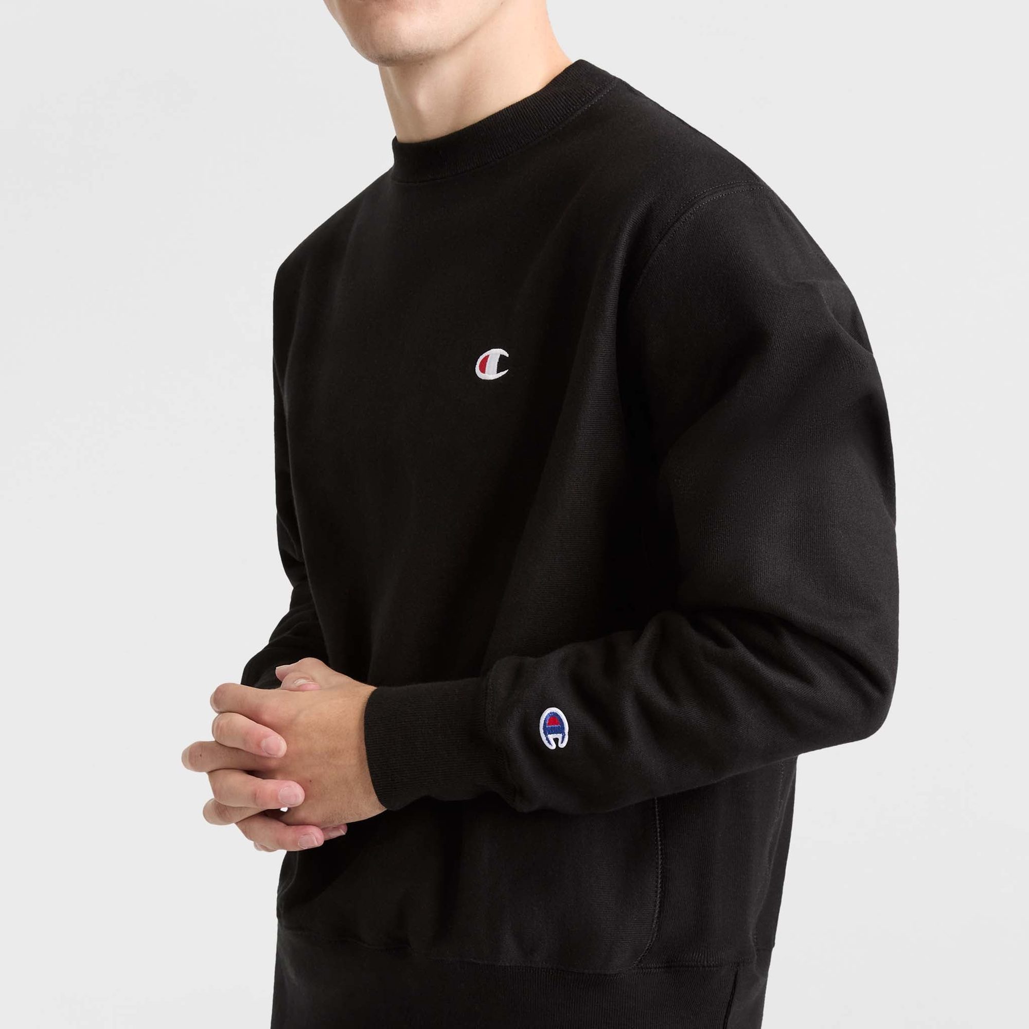 Man wearing black crewneck sweatshirt with small embroidered logo on chest, shown from side
