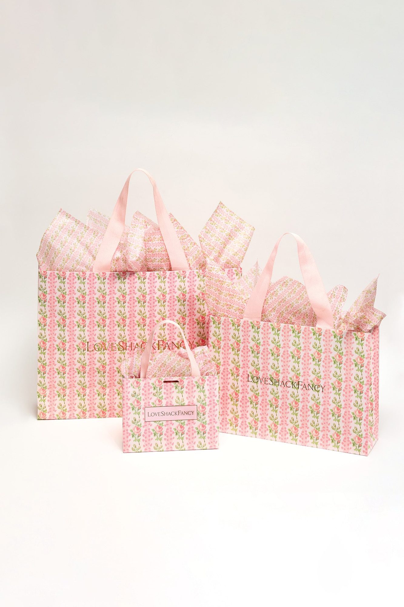 Three sizes of pink floral patterned shopping bags with ribbon handles