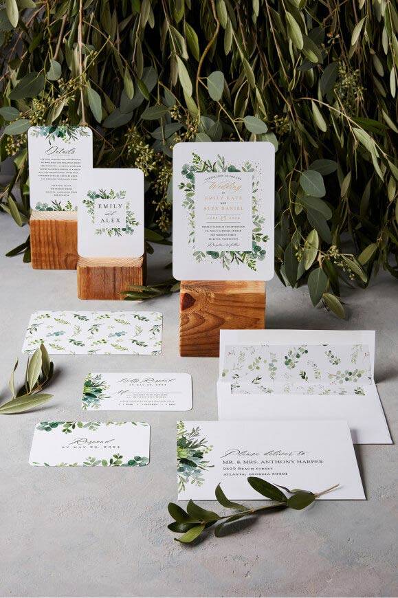 Wedding stationery suite with greenery botanical designs displayed with wooden card holders and eucalyptus branches.