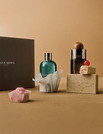 Minimalist beauty display featuring a teal fragrance bottle, soap bars, and a dark branded box on neutral beige background