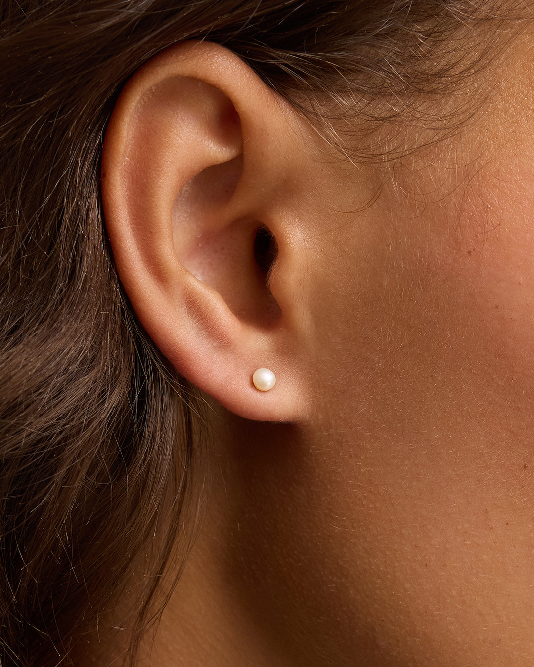 Close-up of woman's ear wearing a single small pearl stud earring