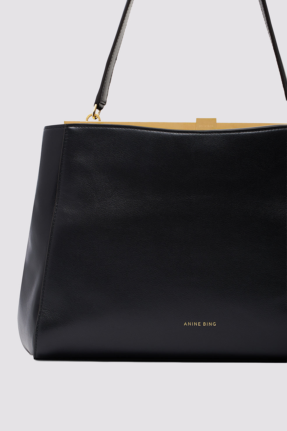 Black leather shoulder bag with gold clasp and 'Anine Bing' text visible, displayed with shoulder strap